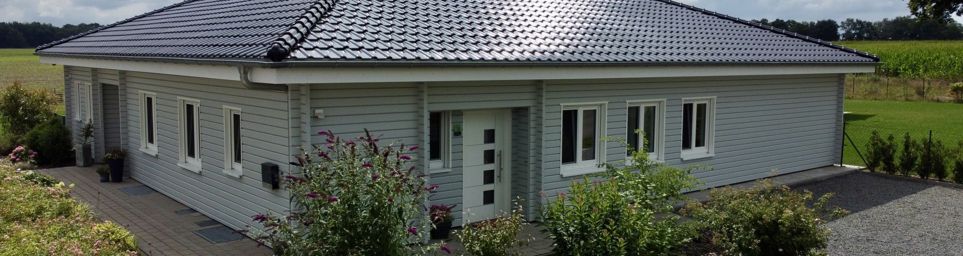 Modernes Holzhaus im Bungalowstil mit hellgrauer Fassade, Walmdach und gepflegtem Garten – Symbol für nachhaltiges Wohnen und Lebensqualität auf einer Ebene